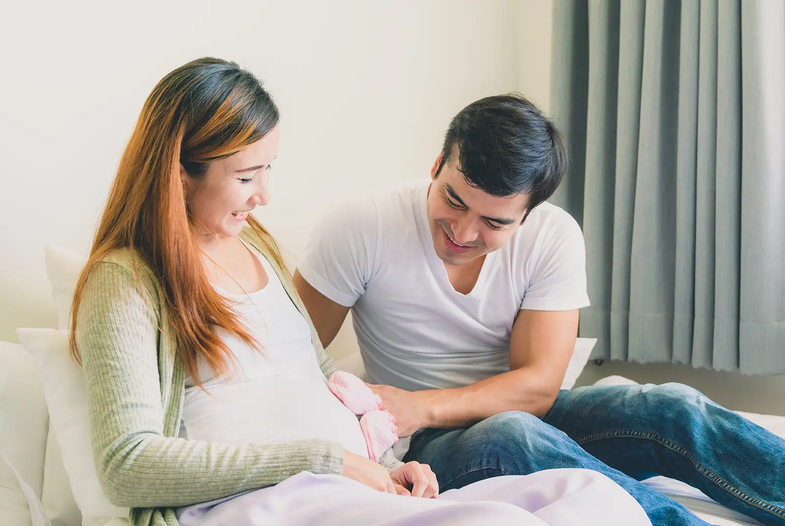 Smiling husband placing baby gloves on pregnant woman's belly